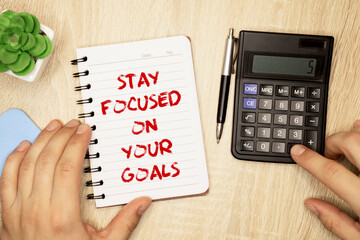 Inspirational quote - Stay focused on your goals. With a text message on a pink sticker on a green notepad.