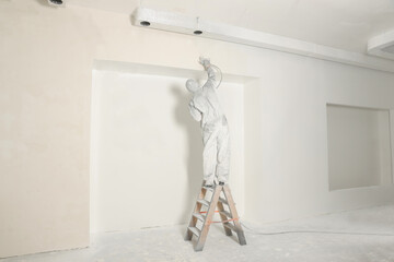 Sticker - Decorator in protective overalls painting wall with spray gun indoors