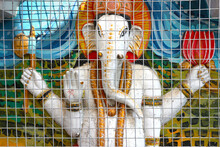 The Four-armed Hindu God Ganesha With The Head Of An Elephant Behind Bars On The Wall Of The Temple. India.