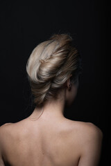  Natural beauty, make-up and fashion concept. Beautiful woman portrait with naked shoulders and hair bun. Model standing back to camera in black studio background with copy space
