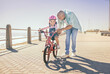 Father, child and bicycle with a girl learning to ride a bike on promenade by sea for fun, bonding and quality time on summer vacation. Man teaching his daughter or girl safety while cycling outdoor