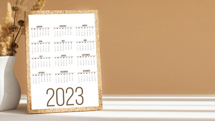 Wall Mural - Calendar for new year 2023 for planners and reminders on desktop next to white vase. Close-up, white-brown background with shadow from rays of sun. Concept of mockup.