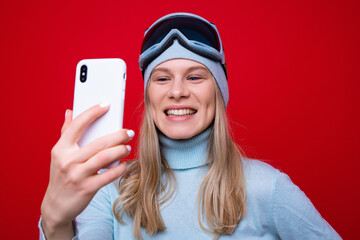 Wall Mural - Portrait of a happy young woman in a sweater and ski goggles taking a selfie.Skiing in the mountains. Studio photos