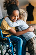 © NDABCREATIVITY - Black little girl with disability in wheelchair hugging with her younger brother.