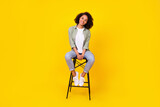 Full body photo of millennial brunette lady sit on chair wear shirt jeans boots isolated on yellow background