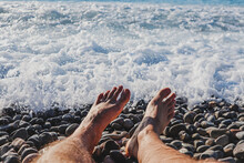 Man's Feet On The Pebble Beach In Fron Of The Sea