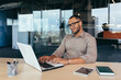© Liubomir - African american programmer at work with laptop inside office, man in glasses and casual writing code for programs.