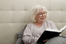 Cheerful Senior Woman Reading Book On Bed