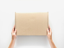 Female Hands Holding A Cardboard Box On A White Background. Packaging And Delivery Concept, Top View