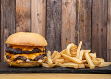 American Food. Closeup View Of A Monster Burger With Meat, Cheddar Cheese And Onion With French Fries.  