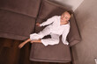 © Шамиль Алиев - A young girl in a homemade white suit barefoot sitting on a brown sofa in the room