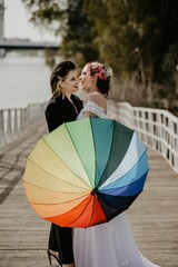 Wall Mural - Vertical closeup of a lesbian pair a bride and a female in black holding a rainbow umbrella