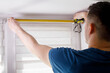 A handyman with a tape measure installs white roller blinds indoors. Shutters day and night