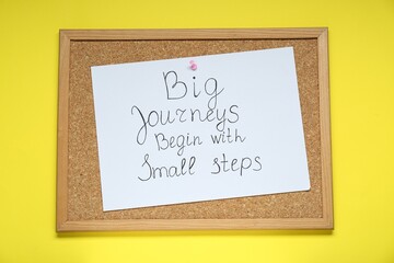 Wall Mural - Corkboard with pinned message Big Journeys Begin With Small Steps on yellow background, top view. Motivational quote