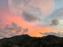 Huge Pink Moon Moves Across Bright Sky, Tinted With Glow Of Sunset, Towards The Horizon. Hilly Area. Green Dense Forest. Thick Clouds Of Fog Rise Above The Trees. Beautiful Landscape. Fantastic Valley