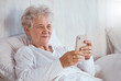 © David L/peopleimages.com - Bed, phone and relax senior patient search internet, web or online for subscription movie, show or entertainment. Healthcare, elderly care and old woman streaming video in retirement nursing home