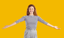 Portrait Of A Happy, Glad, Cheerful, Positive, Friendly Woman With A Kind, Sincere, Toothy Smile Standing On A Yellow Studio Background, Spreading Her Arms Wide Open To Hug You And Give A Warm Welcome