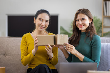 Two Asian women to Startup small business SME entrepreneur of freelance working on laptop computer with parcel box on table laptop at home, online marketing packaging and delivery SME idea concept