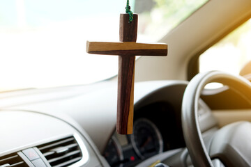 Closeup wooden crucifix hang  in  front steering wheel and console of the car. Concept, talisman,amulet to prevent accidents. Belief, faith,holy  in god to protect when driving.  