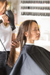 © Виктория Попова - The hairdresser dries the client's hair with a hair dryer and styles her hair with a comb.