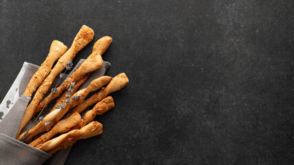 Crispy breadsticks with parmesan and lavender, grissini, on black stone background, top view, place for text, banner