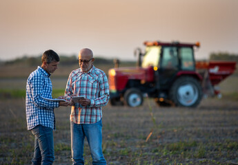 Two farmers in field with tractor in background