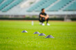 An obstacle cone set on the grass pitch for dribbling training with a player resting as blur background. Professional football training concept, close-up and selective focus on the front cone. 
