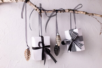 Wrapped black and white boxes with presents and decorative cones hanging on a branch against textured background. Scandinavian style. Place for text.