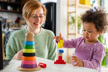 Mother looking at a child playing with an educational didactic toy. Young woman and child playing with didactic toys