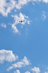 Wall Mural - The passenger plane is flying far away in the blue sky and white clouds. Airplane in the air. International passenger air transportation. The plane flies in the distance. Vertical illustration