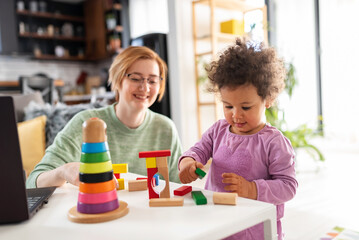 Wall Mural - Mother looking at a child playing with an educational didactic toy. Young woman and child playing with didactic toys