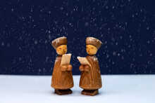 Wooden Cute Carol Singers Figurines Closeup On Holly Night At Christmas With Snow Falling