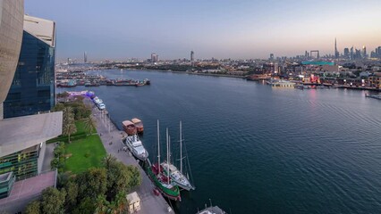 Wall Mural - Dubai creek landscape day to night transition timelapse with boats and yachts and modern buildings with traffic on the road. Aerial top view from above