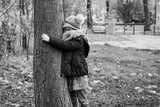 Dziewczynka przytula się do drzewa w parku, kocha przyrodę, jesienny spacer popołudniowy, dziecko w kurtce, czapce i szalu, zima, zimowy spacer