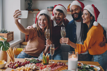 Beautiful people in Christmas hats making selfie and smiling while celebrating at home