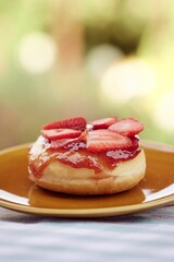 Canvas Print - Tasty donut topped with fresh sliced strawberries on a saucer, vertical shot