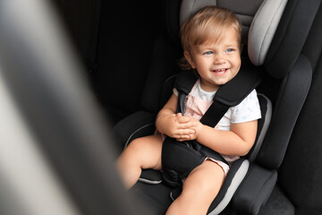 Cute little girl sitting in child safety seat inside car