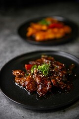 Sticker - Closeup shot of sweet and sticky crispy striped beef on black plate with gray blurry background