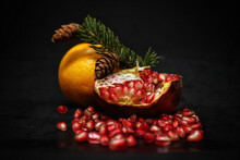 Pomegranate And Tangerine On A Black Background With A Green Sprig Of Spruce