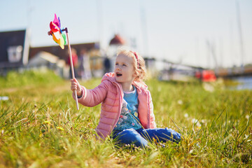 Wall Mural - Adorable preschooler girl with colorful pinwheel walking in picturesque village of Marken, North Holland, the Netherlands