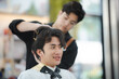 © chokniti - Asian man sitting in customer chair while getting a haircut in salon with a male hair stylist