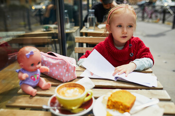 Wall Mural - Adorable preschooler girl drawing in cafe while her mother is drinking coffee