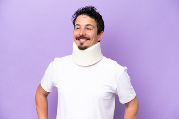 Wall Mural - Young caucasian man wearing neck brace isolated on purple background posing with arms at hip and smiling