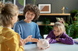 © Mediaphotos - Mother pointing at piggy bank and teaching her children to save money while they sitting at table in the room