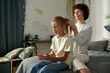 © Mediaphotos - Young mother making hairstyle to her daughter in bedroom, they spending leisure time together