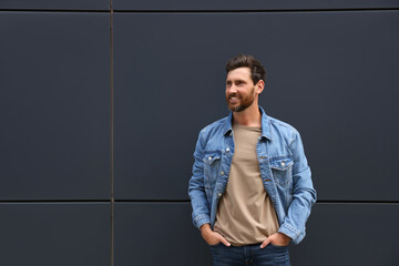 Wall Mural - Smiling handsome bearded man near grey wall outdoors. Space for text