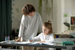 © Mediaphotos - Young mother helping her son with his homework while he sitting at desk in the room