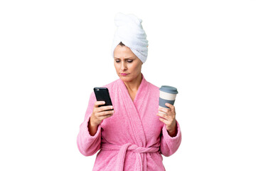 Canvas Print - Middle age caucasian woman in a bathrobe over isolated background holding coffee to take away and a mobile