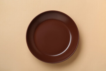 Wall Mural - Empty brown ceramic plate on pale orange background, top view