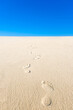 View of yellow sand, blue sky and footsteps disappearing into the distance. Vertical photo of an empty beach.